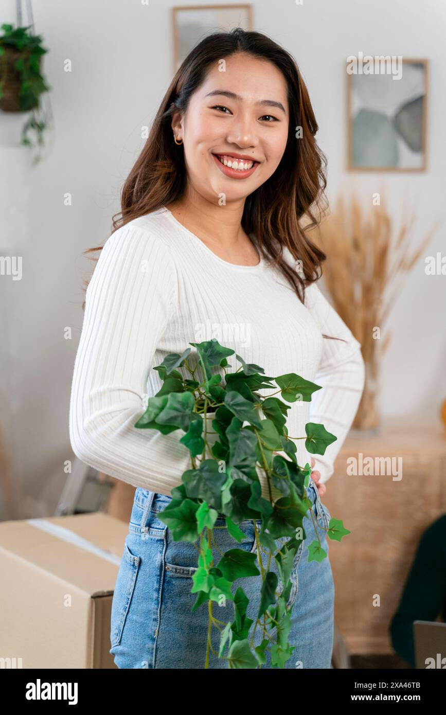 Donna sorridente che tiene una pianta in vaso al chiuso. Foto Stock