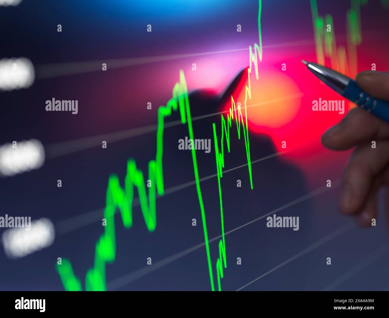 Una mano con una penna punta a un grafico luminoso del mercato azionario su uno schermo digitale con linee fluttuanti verdi e rosse che indicano i dati finanziari. Foto Stock