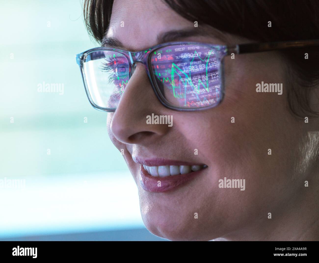 Primo piano di una donna sorridente che indossa occhiali che riflettono un grafico colorato. L'immagine si concentra sul suo profilo, mostrando i suoi occhiali e la sua espressione gioiosa. Foto Stock
