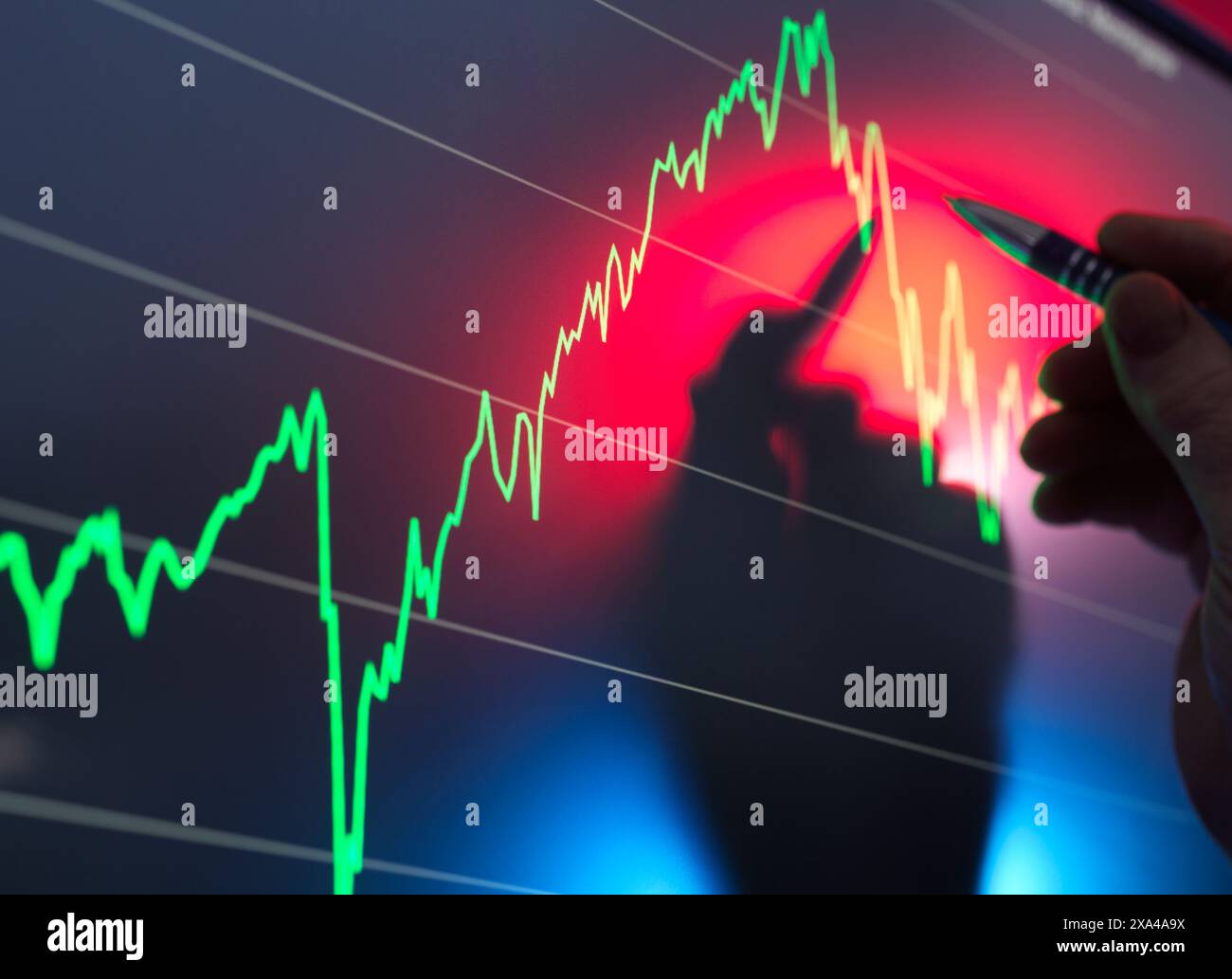 Una persona esamina i dati finanziari su una schermata che visualizza un grafico con i trend verso l'alto e verso il basso, utilizzando una penna per tracciare il grafico lineare. Foto Stock