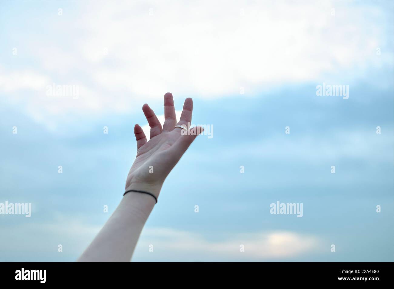 Una mano tesa raggiunge un cielo blu con nuvole mostruose. Foto Stock