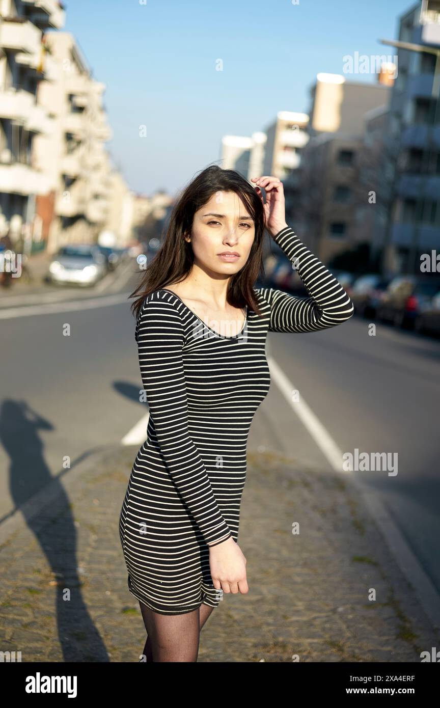 Una donna sta in piedi su una strada della città con la luce del sole che le proietta un'ombra dietro mentre tocca i capelli. Foto Stock