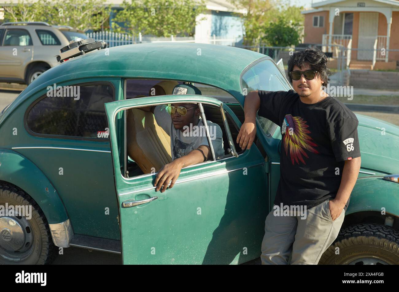 Un adolescente si appoggia su un'auto verde d'epoca, con un altro adolescente seduto al posto di guida; entrambi sono vestiti in modo informale in una giornata di sole. Foto Stock