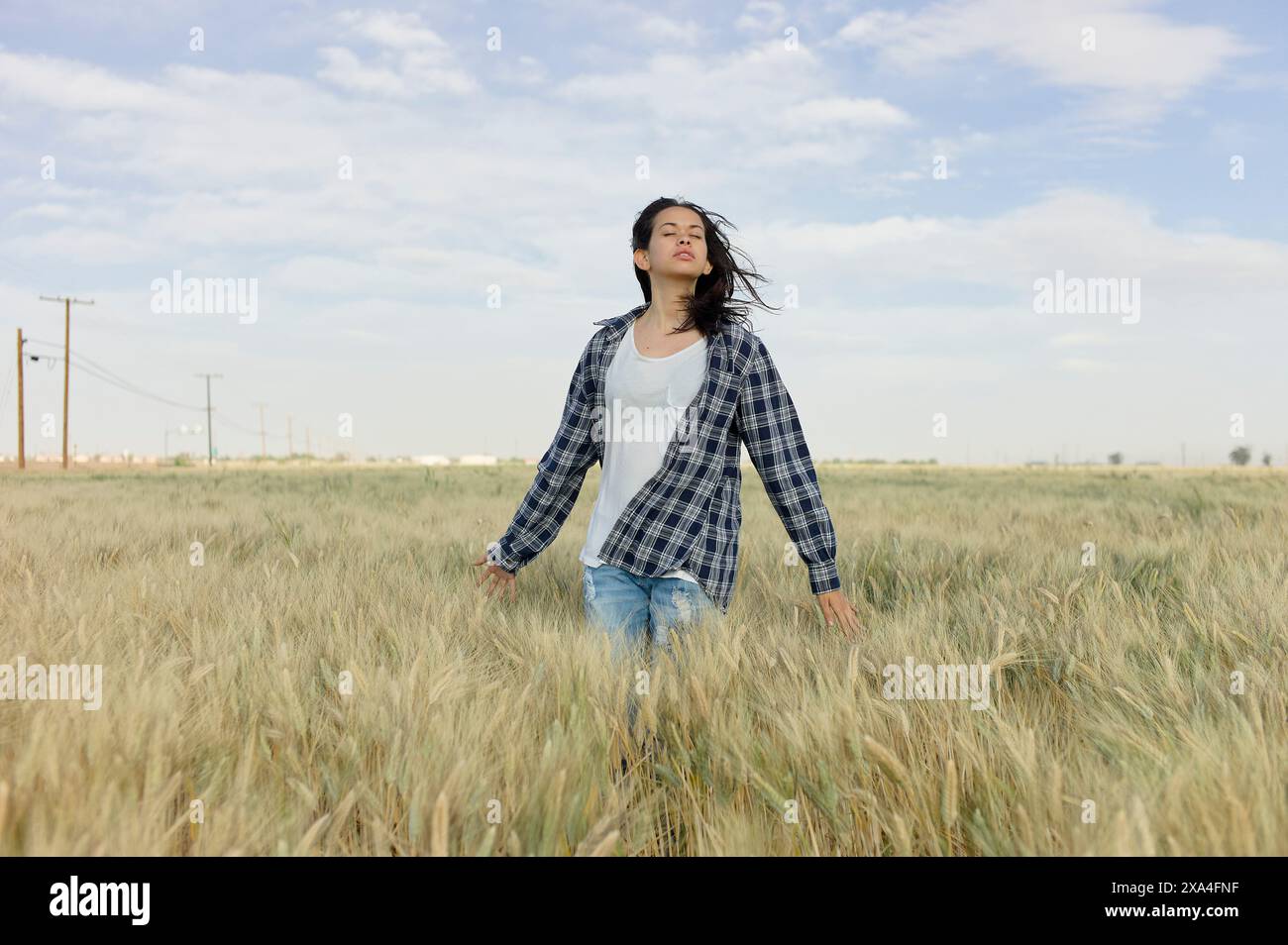 Una donna sta in un campo di grano con le braccia tese e gli occhi chiusi, abbracciando lo spazio aperto. Foto Stock