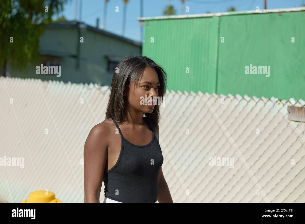 Una donna con i capelli di media lunghezza si trova di fronte a una recinzione a picchetto bianca, con uno sfondo verde e un cielo azzurro. Foto Stock