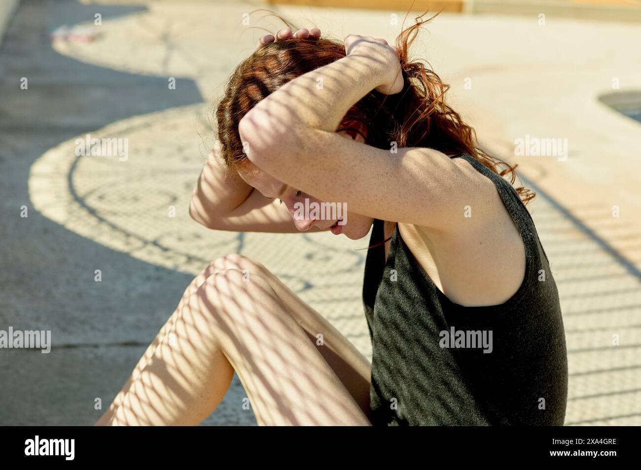 Una donna seduta all'aperto a terra protegge il viso dal sole con il braccio. Foto Stock