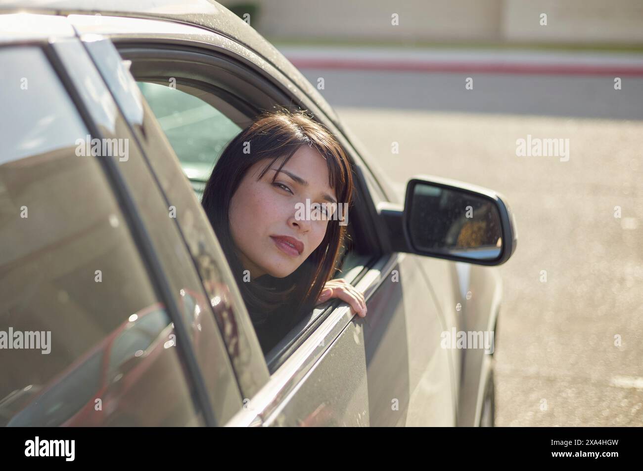 Una donna dai capelli scuri guarda fuori dal finestrino di un'auto parcheggiata, con un'espressione mirata sul suo volto. Foto Stock