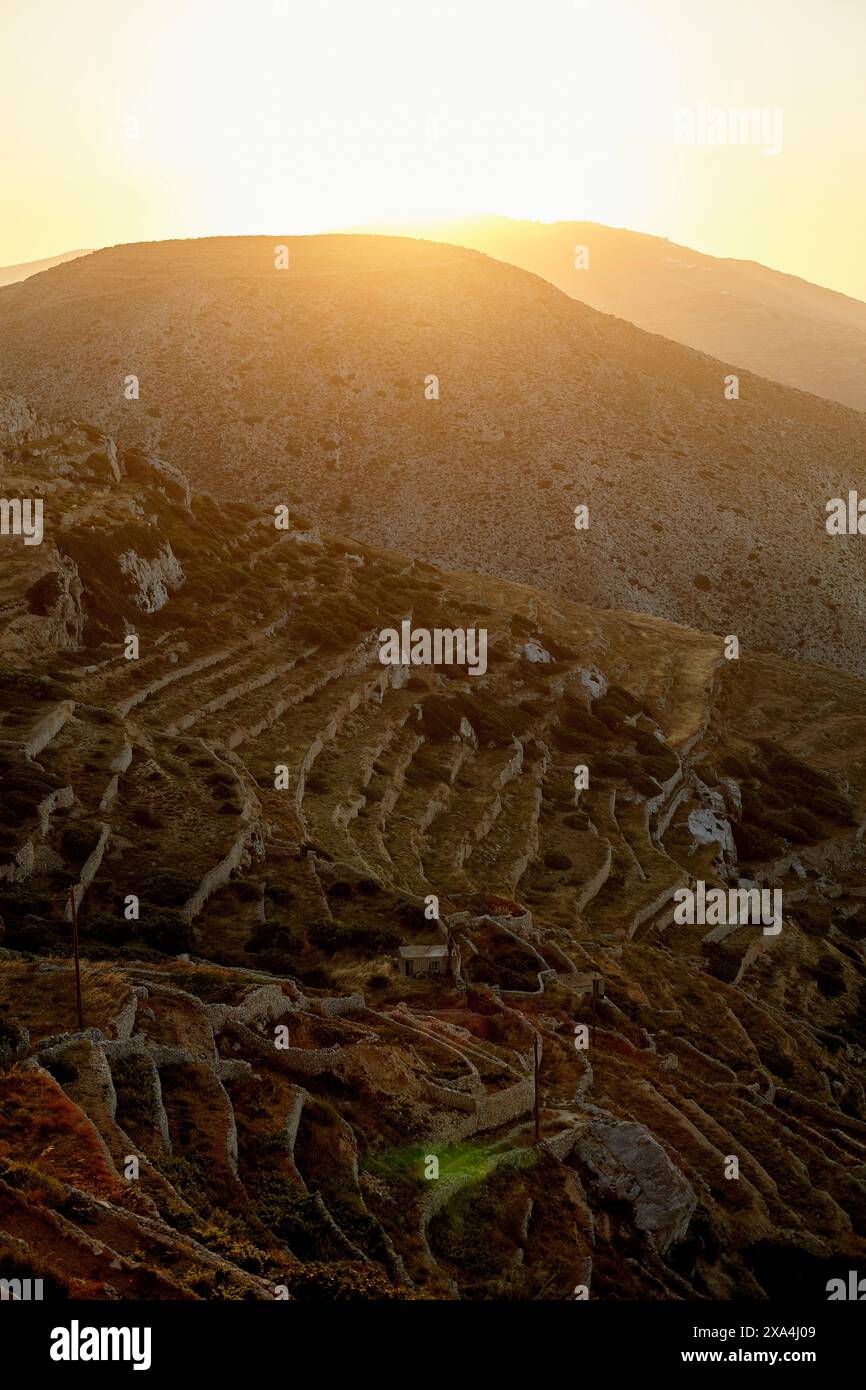 Il sole tramonta dietro una collina, emettendo un caldo bagliore su pendii terrazzati con una rete di sentieri o gradini scavati nel paesaggio. Foto Stock