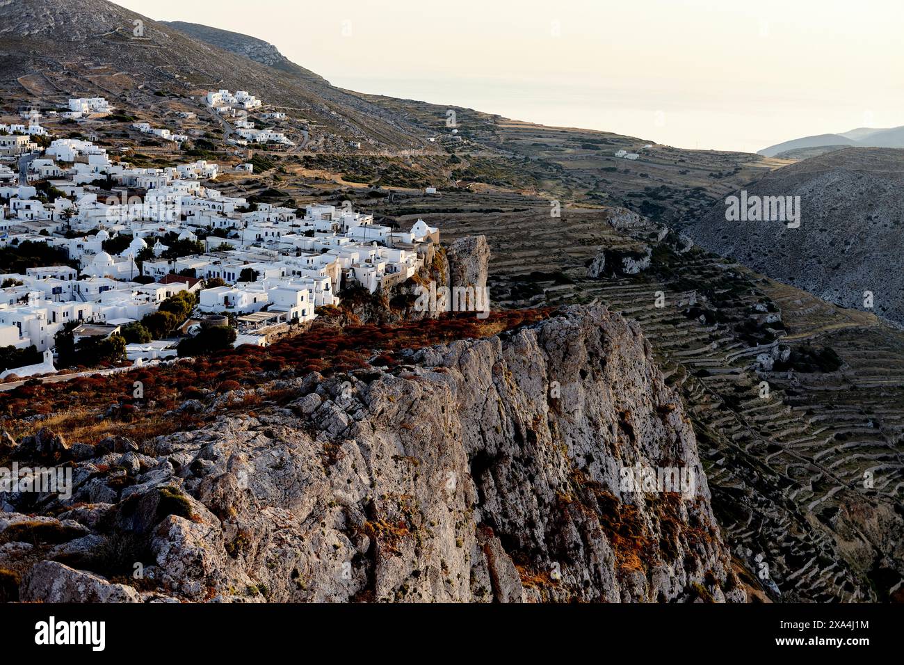 Una vista panoramica di un tradizionale villaggio bianco annidato in aspre colline, bagnato dal caldo bagliore del sole che tramonta. Foto Stock