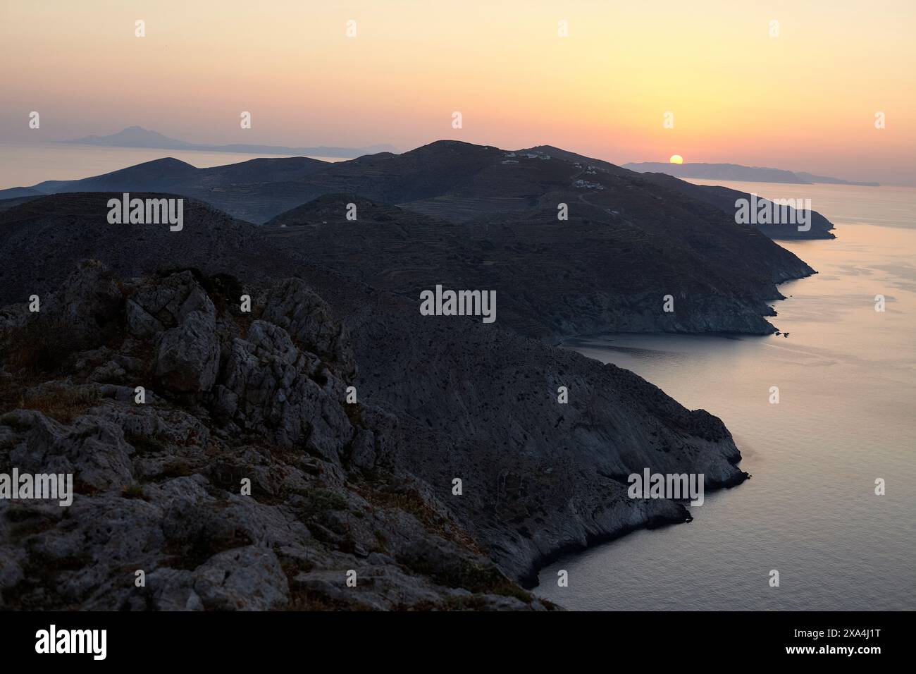 Il sole tramonta dietro una costa montuosa, che getta un caldo bagliore sul tranquillo paesaggio marino. Foto Stock