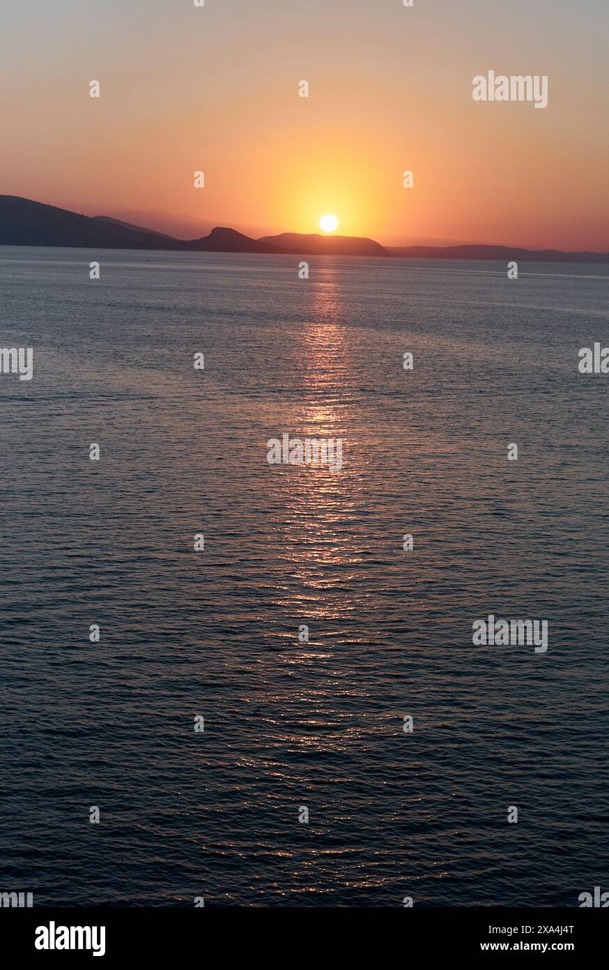 L'immagine cattura un tramonto sereno con il sole che si alza appena sopra l'orizzonte, proiettando un caldo bagliore e un percorso riflettente sull'acqua. Foto Stock