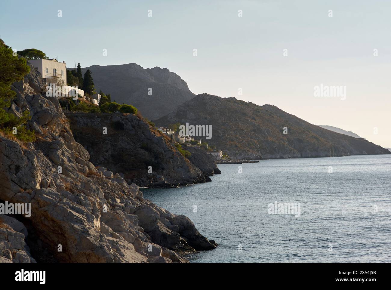 Un tranquillo paesaggio costiero caratterizzato da una costa frastagliata con edifici arroccati in cima alle scogliere, che si affacciano su un mare calmo con montagne sullo sfondo al crepuscolo. Foto Stock
