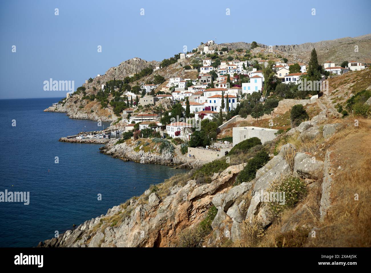 Un pittoresco villaggio costiero con edifici bianchi accoccolati su una collina che si affaccia su un mare blu calmo. Foto Stock