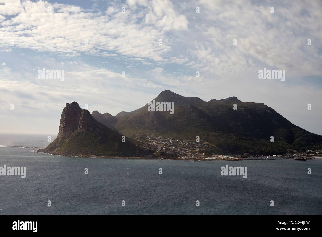 Paesaggio costiero caratterizzato da una cittadina di mare annidata alla base di una spettacolare catena montuosa sotto un cielo parzialmente nuvoloso. Foto Stock