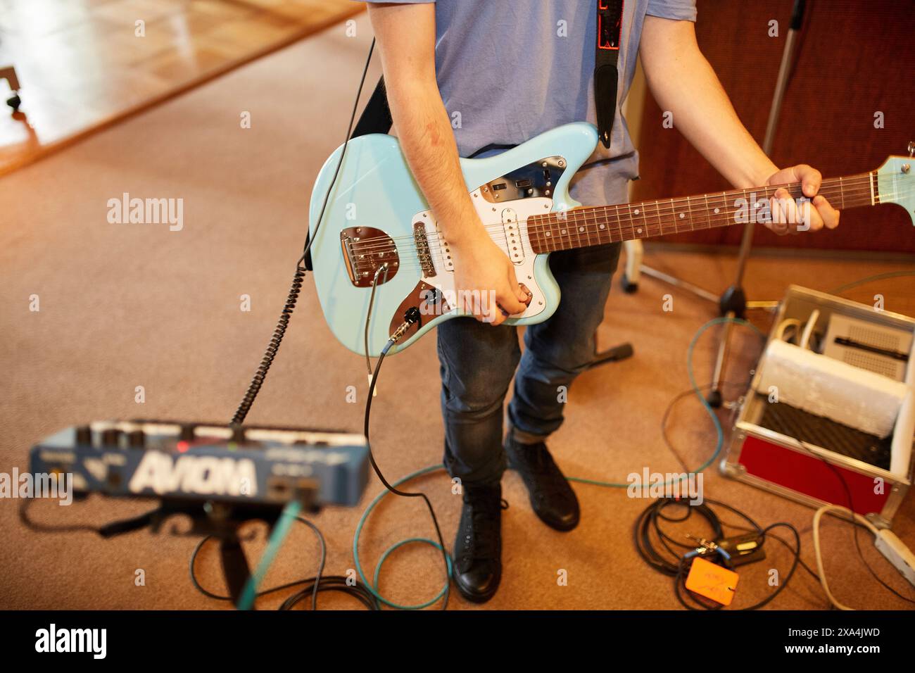 Una persona in piedi mentre suona una chitarra elettrica, circondata da attrezzature musicali tra cui pedali e un amplificatore. Foto Stock