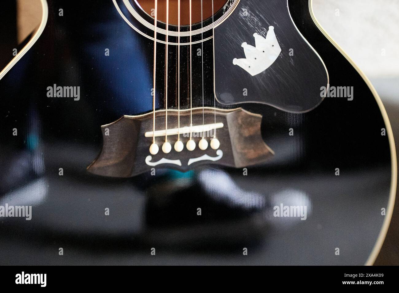 Questa è una foto ravvicinata di una chitarra acustica nera che mostra le corde, il buco del suono e il ponte, con un riflesso visibile sul corpo. Foto Stock