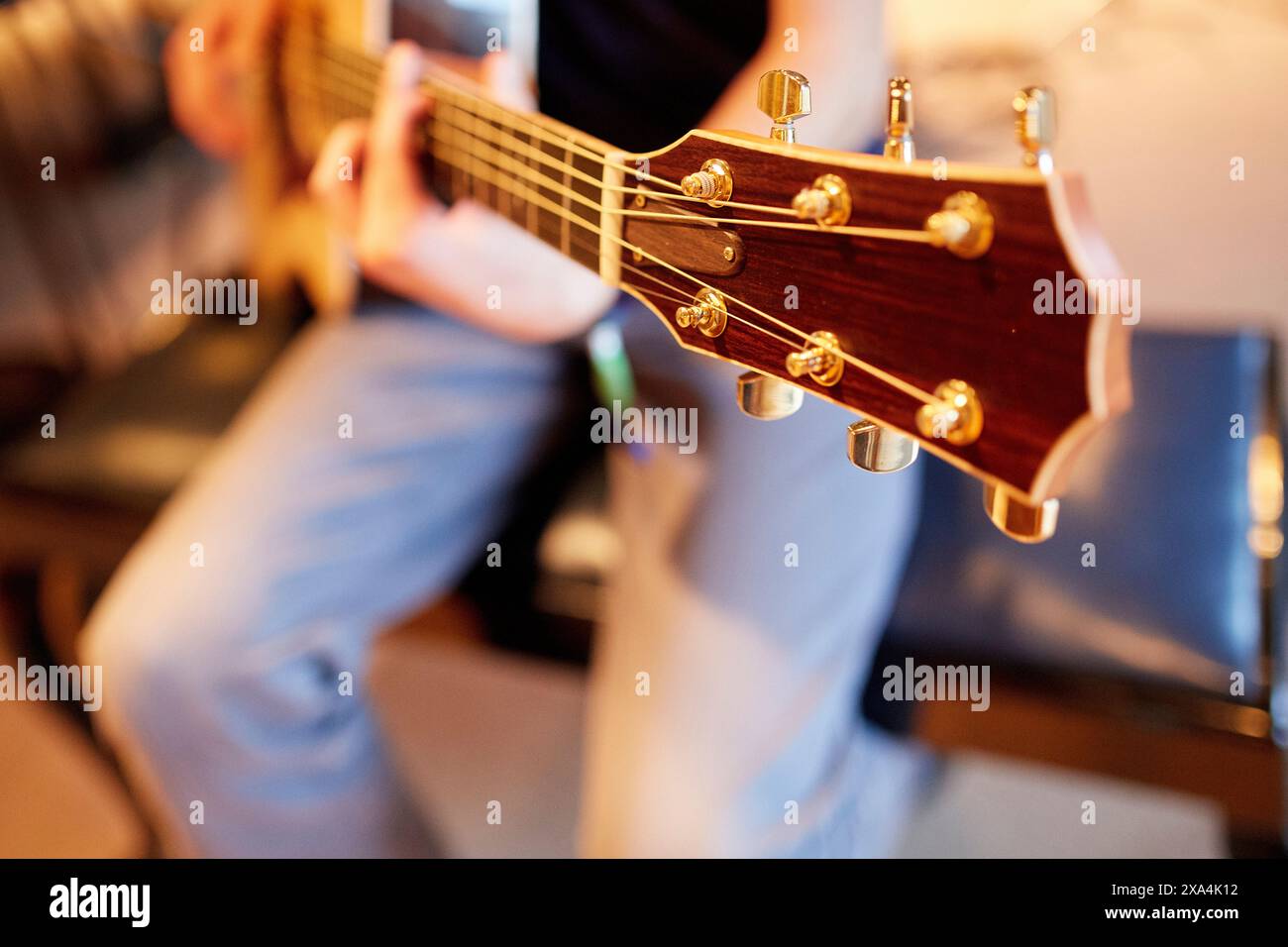 Un primo piano di una paletta di chitarra in esecuzione, con particolare attenzione ai piedini di sintonizzazione e alle mani e alle corde sfocate sullo sfondo. Foto Stock