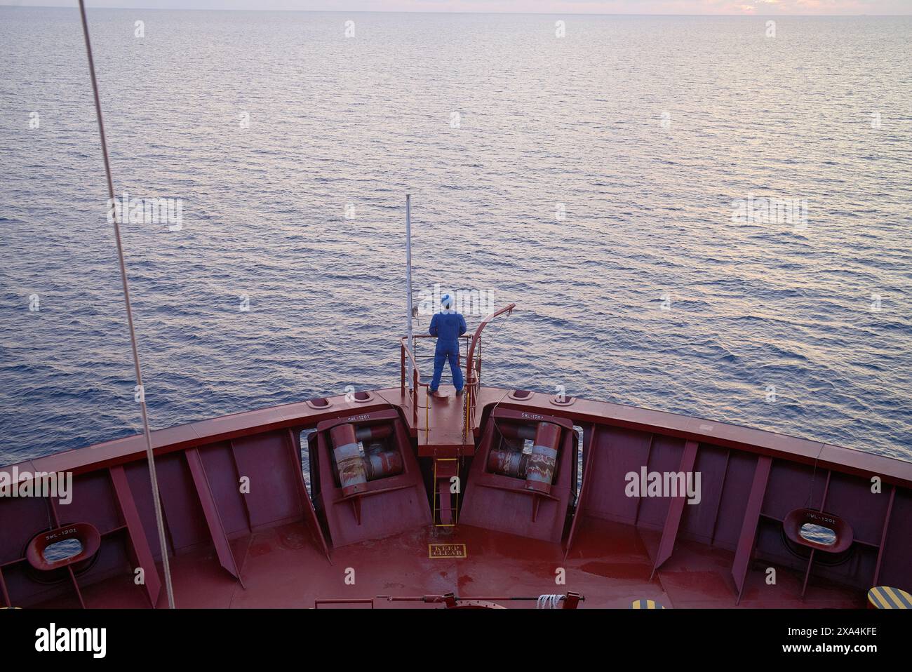 Una persona sta sulla prua di una nave rossa, guardando il mare blu calmo durante il tramonto. Foto Stock