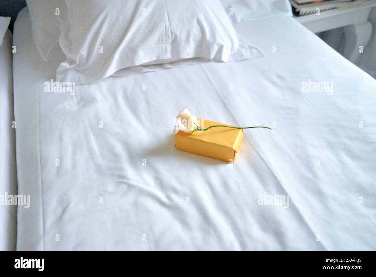 Un letto ben fatto con biancheria bianca, con un omaggio singolo avvolto con nastro giallo al centro. Foto Stock