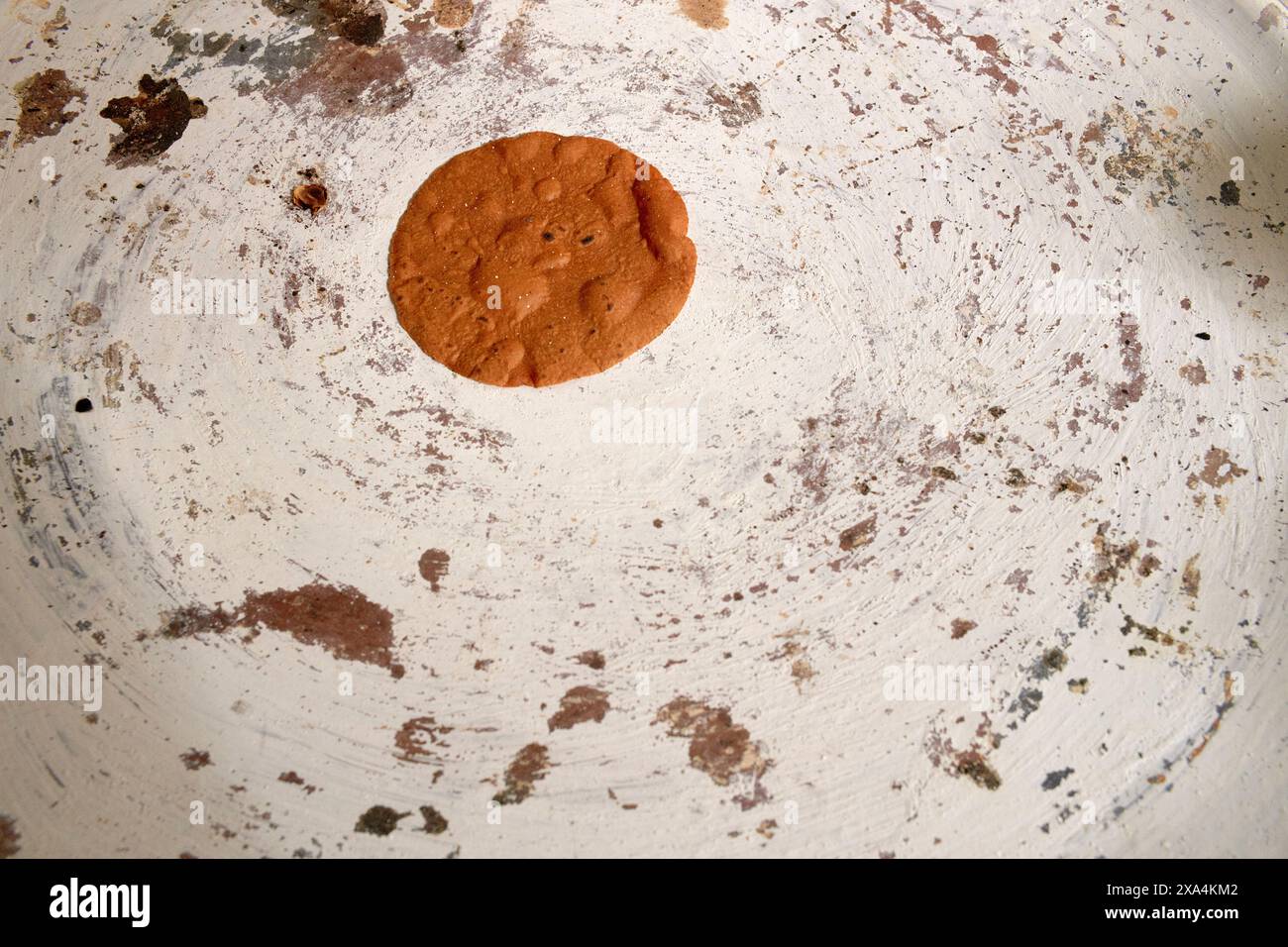 Un unico biscotto con gocce di cioccolato appena sfornato si trova al centro di una teglia da forno ben utilizzata e invecchiata con residui di biscotti intorno. Foto Stock