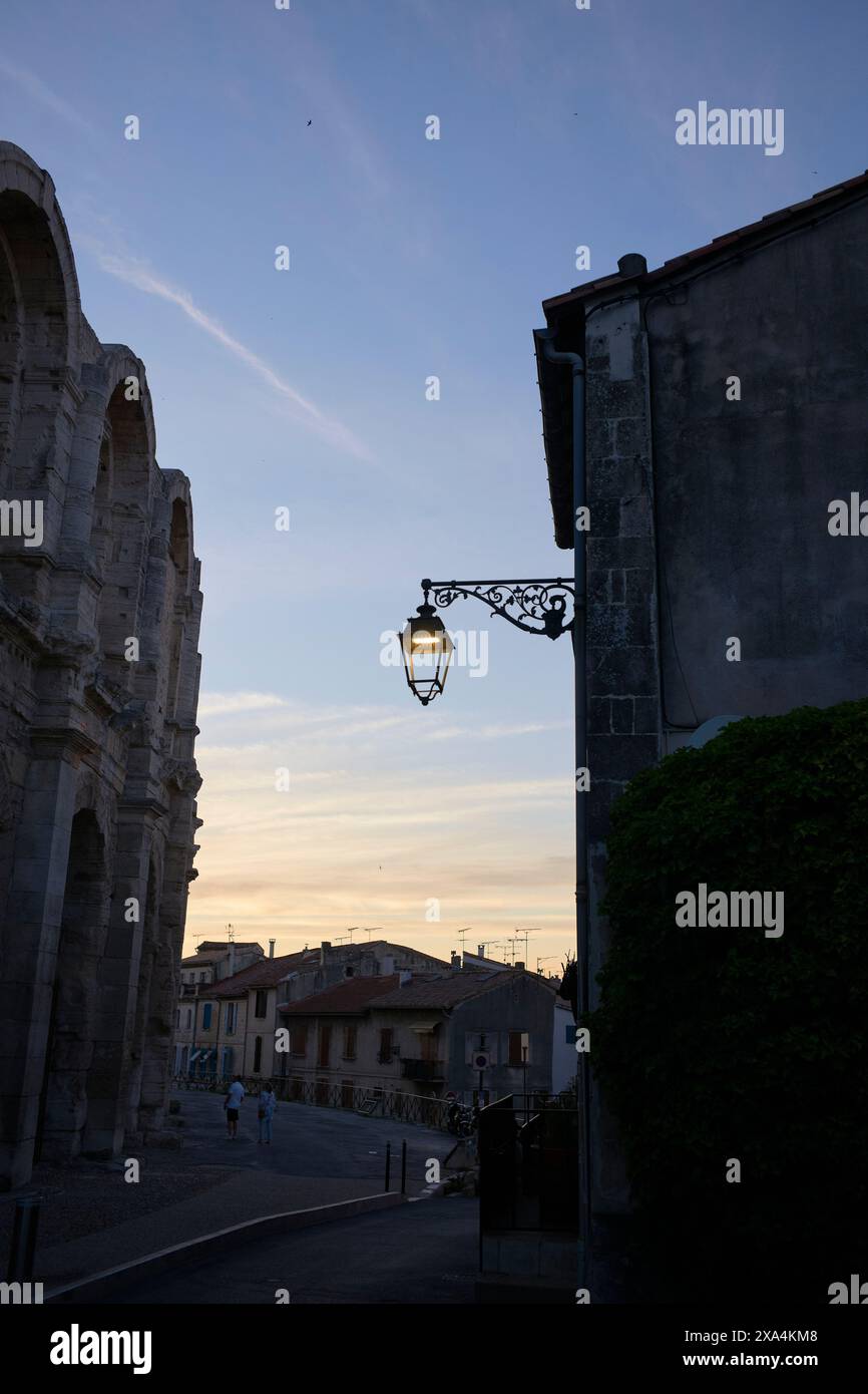 Una lampada da strada in vecchio stile si staglia contro un cielo crepuscolo accanto a un antico edificio in pietra con un tocco di fogliame. Foto Stock