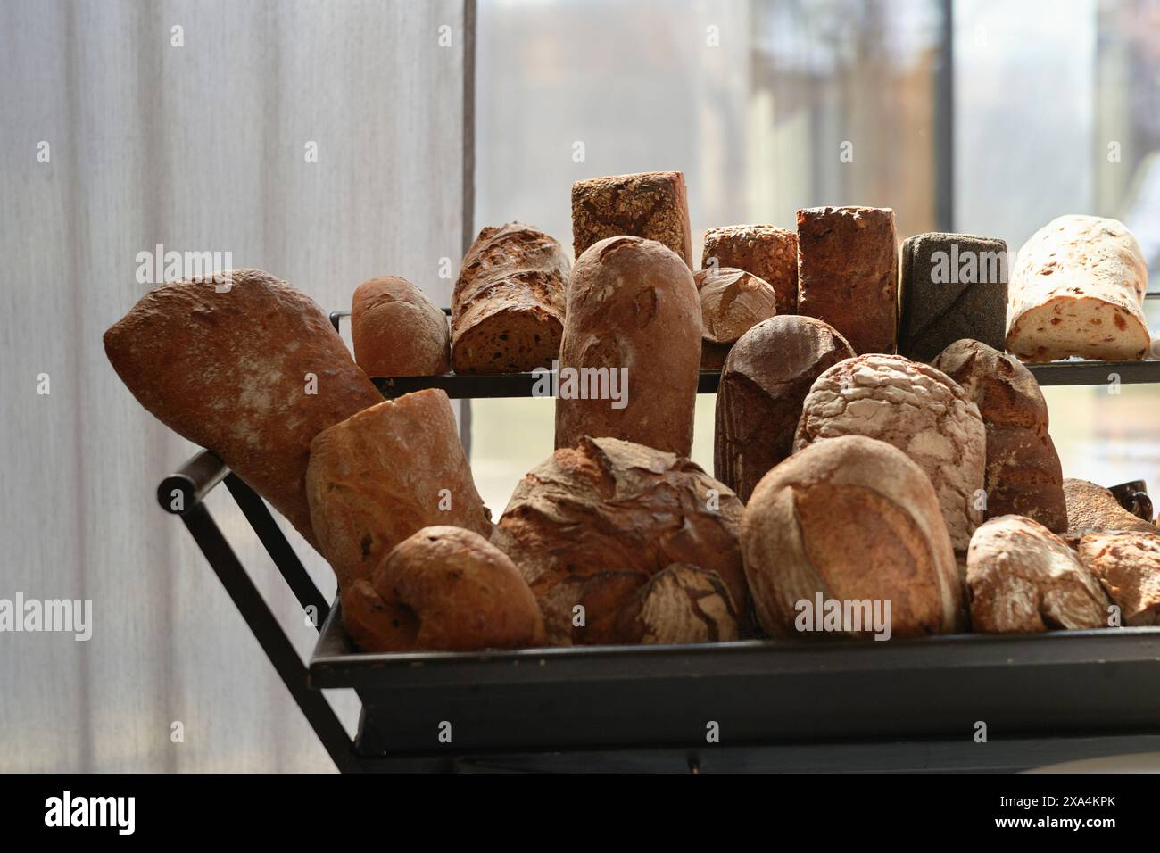 Una varietà di pani appena sfornati esposti su uno scaffale, che proiettano ombre morbide in un ambiente caldo e illuminato. Foto Stock