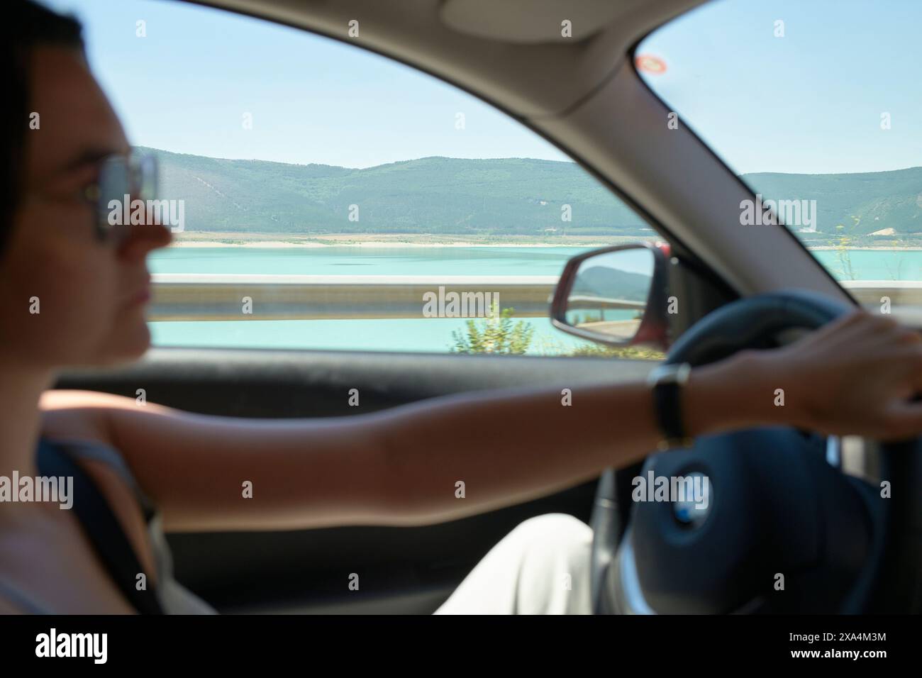 Una donna sta guidando un'auto con un paesaggio panoramico visibile attraverso i finestrini, concentrandosi sulla strada davanti. Foto Stock