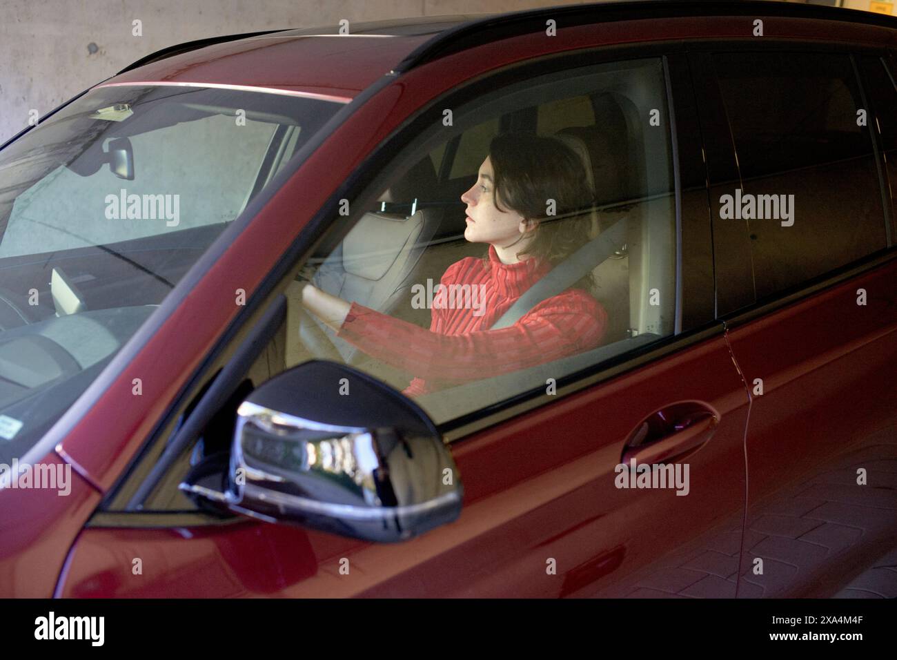 Un individuo concentrato guida un'auto rossa attraverso un garage. Foto Stock