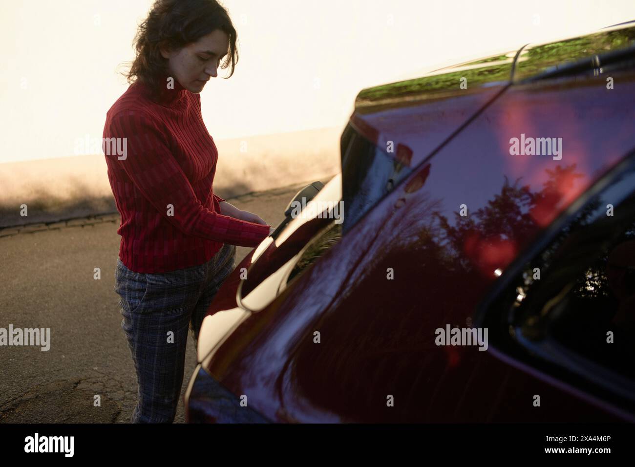 Una persona sta aprendo la porta di un'auto durante una serata di sole, proiettando un caldo bagliore sulla scena. Foto Stock
