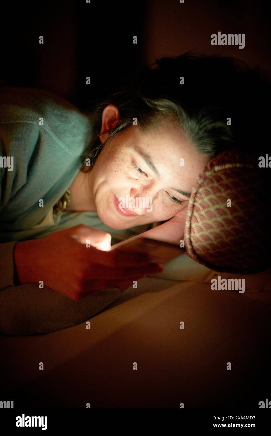 Una donna sta appoggiando la testa sulla mano e sorride dolcemente mentre guarda una sorgente luminosa che offre un'atmosfera calda. Foto Stock