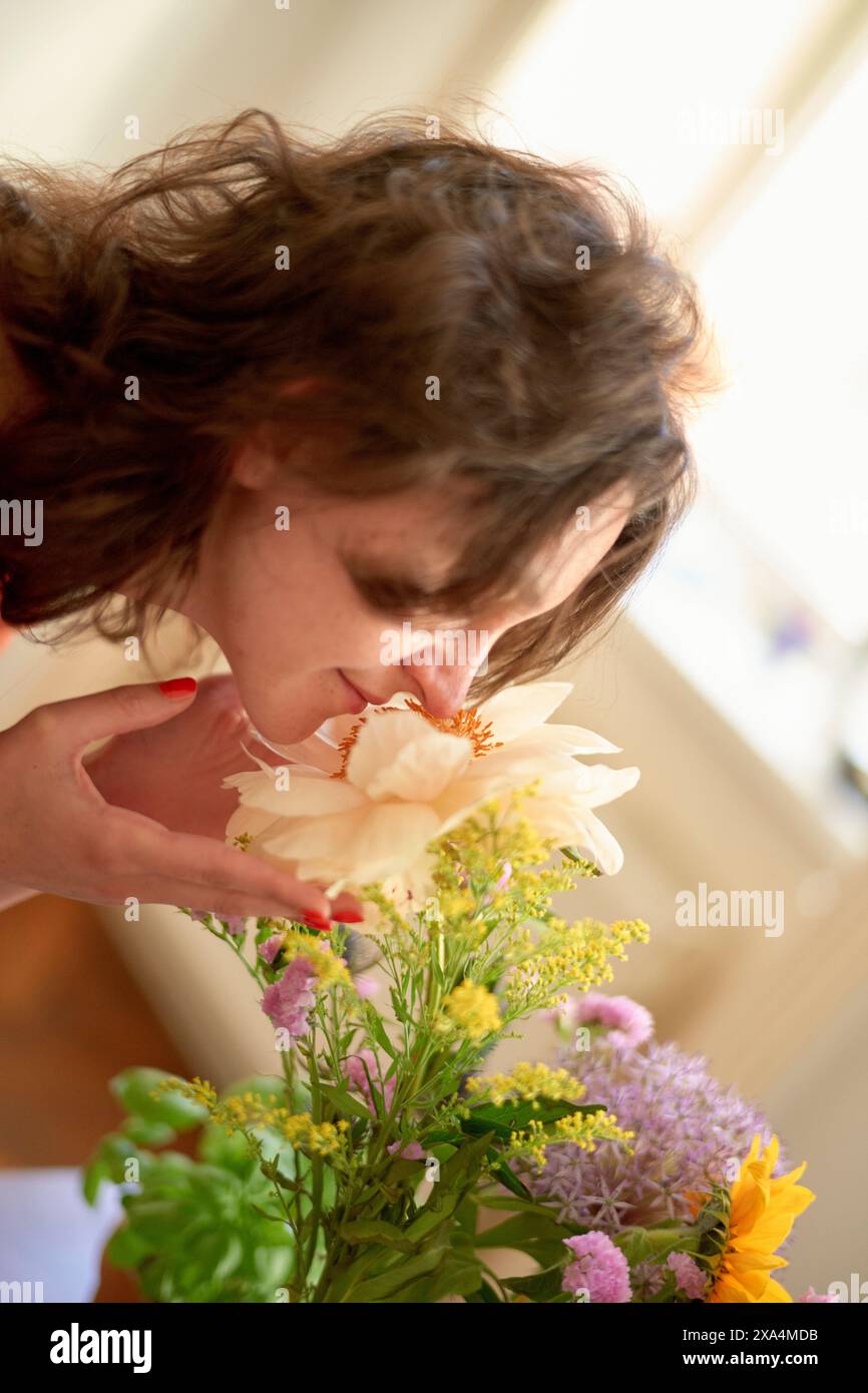 Una donna odora delicatamente un fiore color crema in un bouquet con vari altri fiori dai colori vivaci su sfondo morbido e focalizzato. Foto Stock