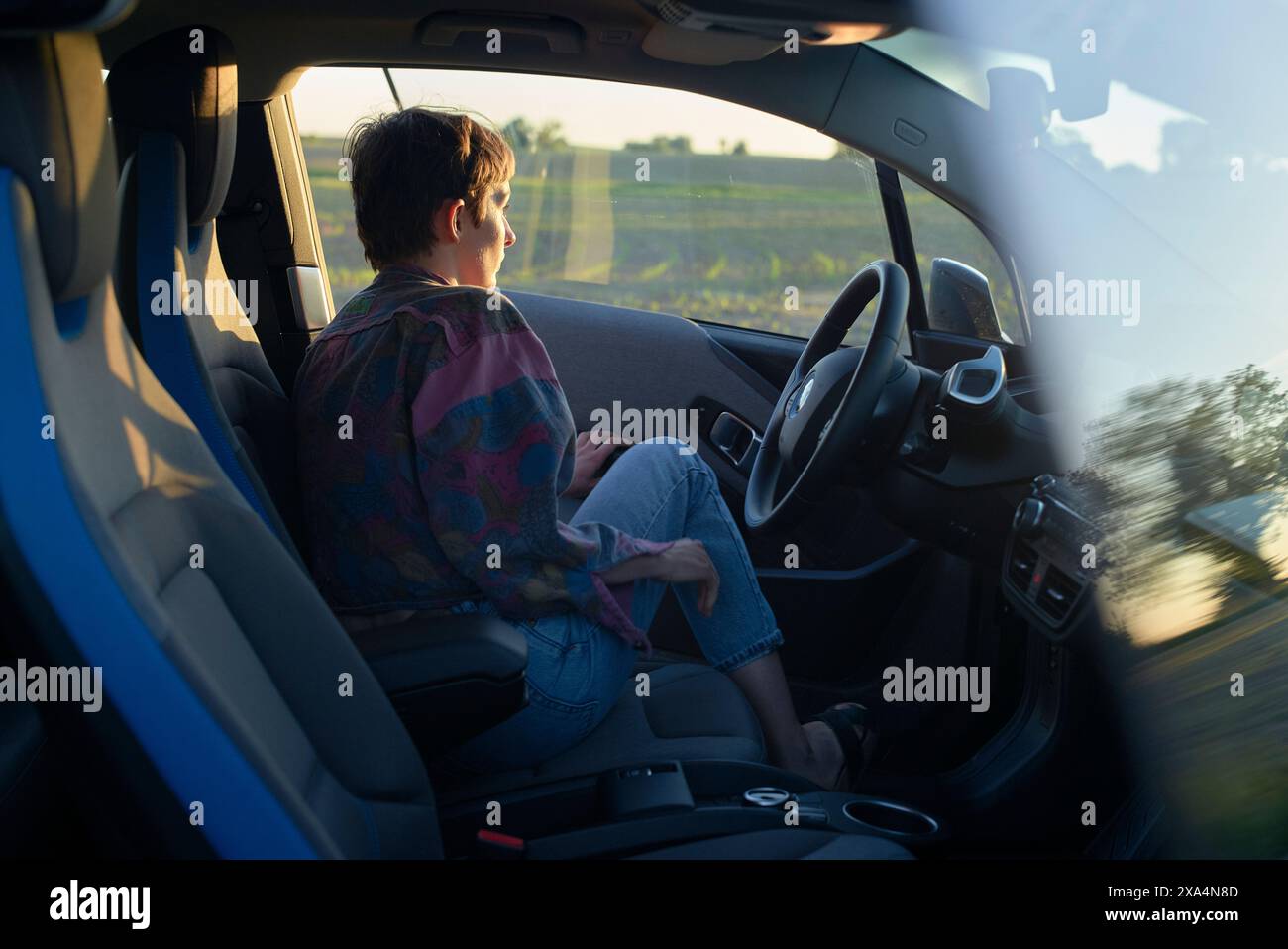 Una giovane donna viene vista guidare un'auto durante quella che sembra essere la prima sera, con il sole dorato che getta luce soffusa sul suo profilo. Foto Stock