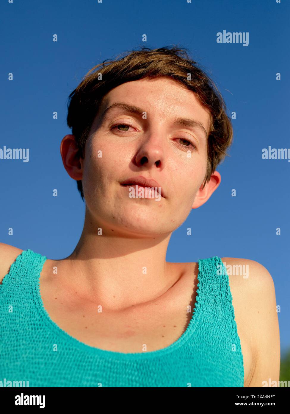 Ritratto ravvicinato di una giovane donna dai capelli corti che guarda la fotocamera con un cielo blu chiaro sullo sfondo. Foto Stock