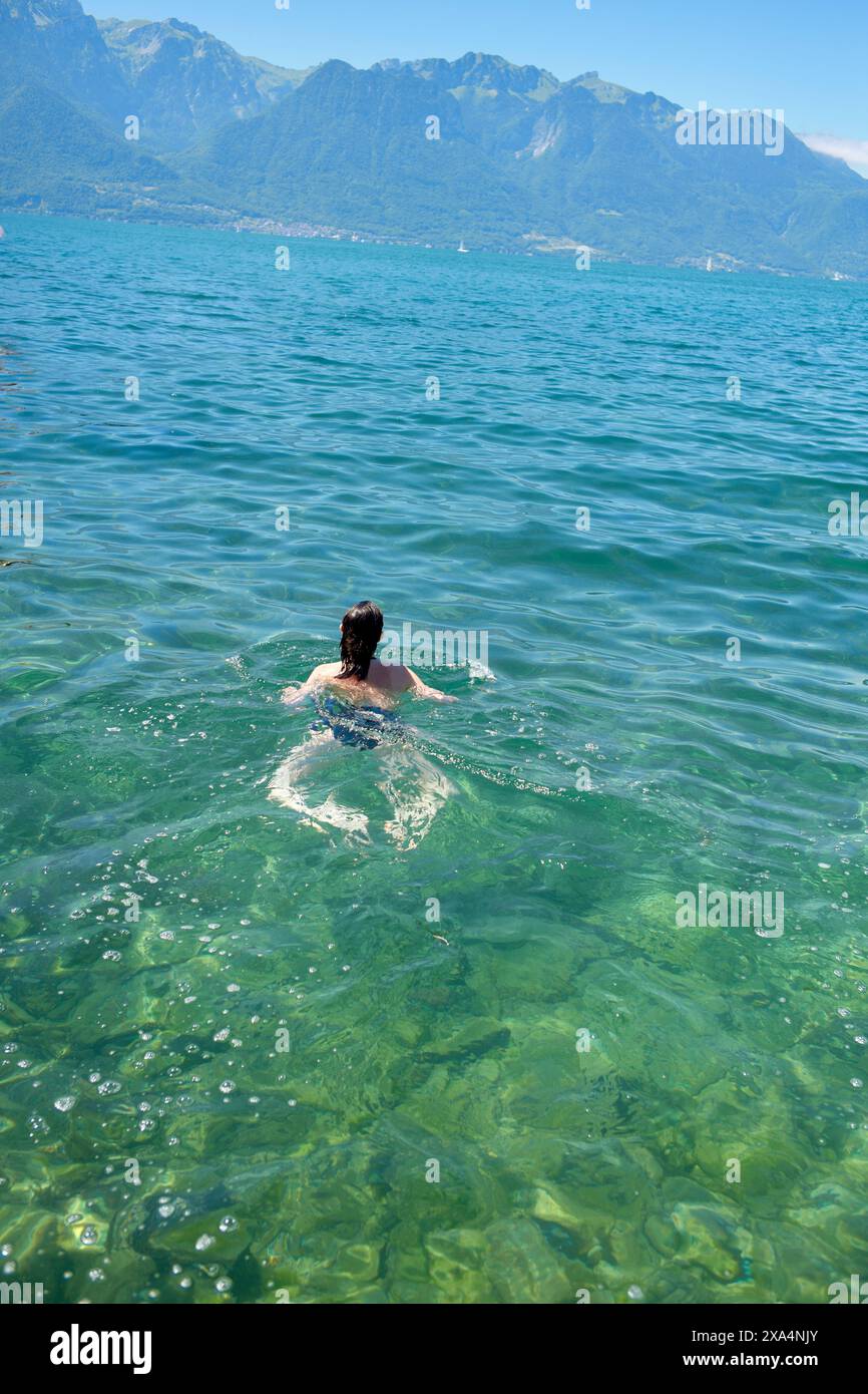 Un nuotatore gode delle limpide acque turchesi di un tranquillo lago con vista sulle montagne sullo sfondo. Foto Stock