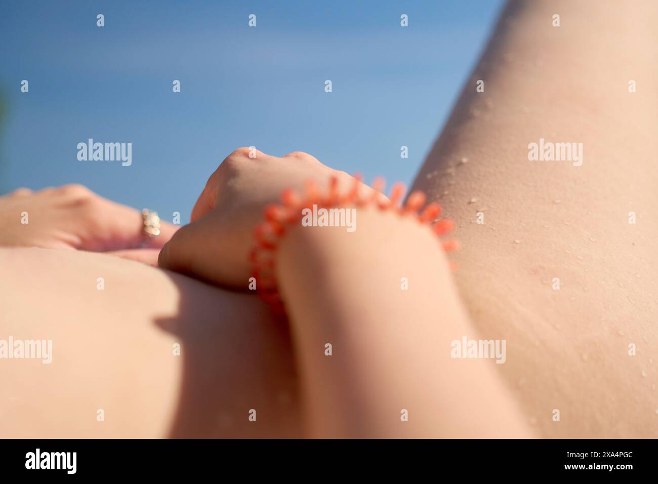 Primo piano della pelle baciata dal sole di una persona con un braccialetto a spirale rosso e un anello al dito, su uno sfondo blu chiaro. Foto Stock