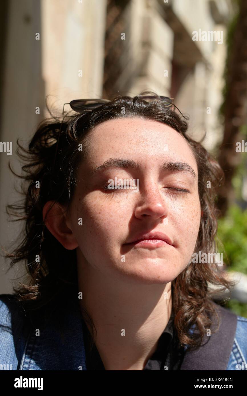 Una giovane donna con gli occhi chiusi si crogiola alla luce del sole, creando ombre ad alto contrasto sul viso. Foto Stock