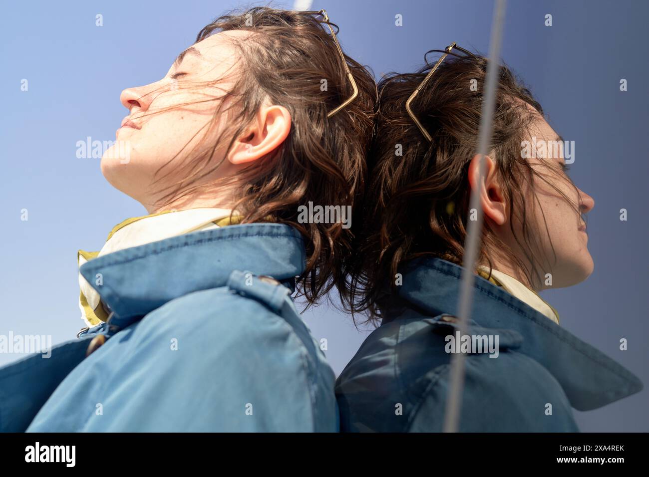 Primo piano di una giovane donna con il vento tra i capelli che indossa giacche blu abbinate Foto Stock