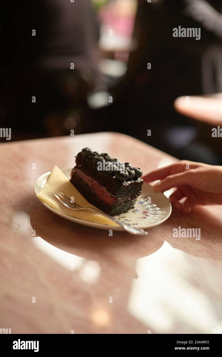 Fetta di torta al cioccolato adornata con frutti di bosco su un piatto con un dito umano che lo tocca delicatamente. Foto Stock