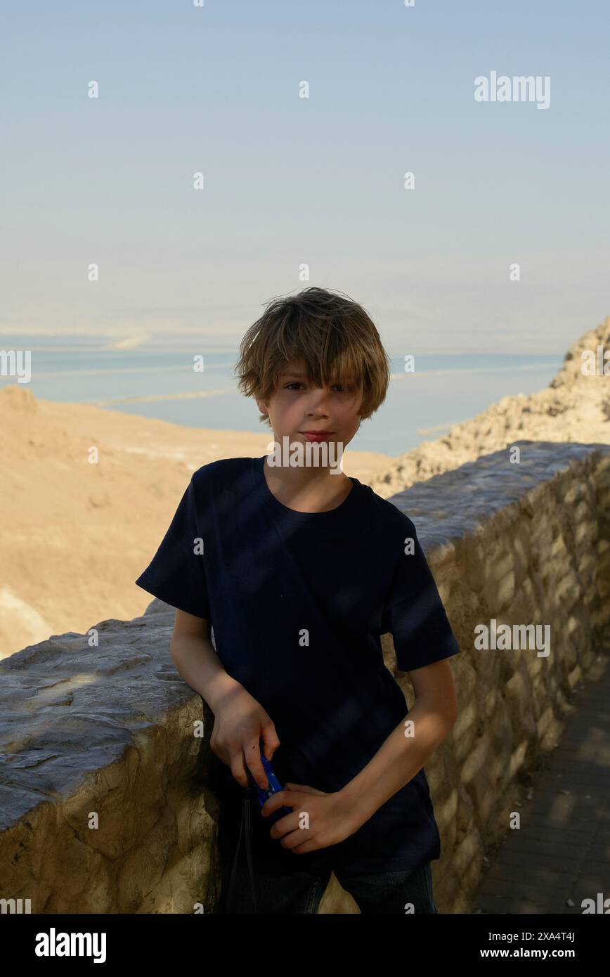 Ragazzino con i capelli arrugginiti in piedi accanto a un muro di pietra che si affaccia su un tranquillo paesaggio acquatico. Foto Stock