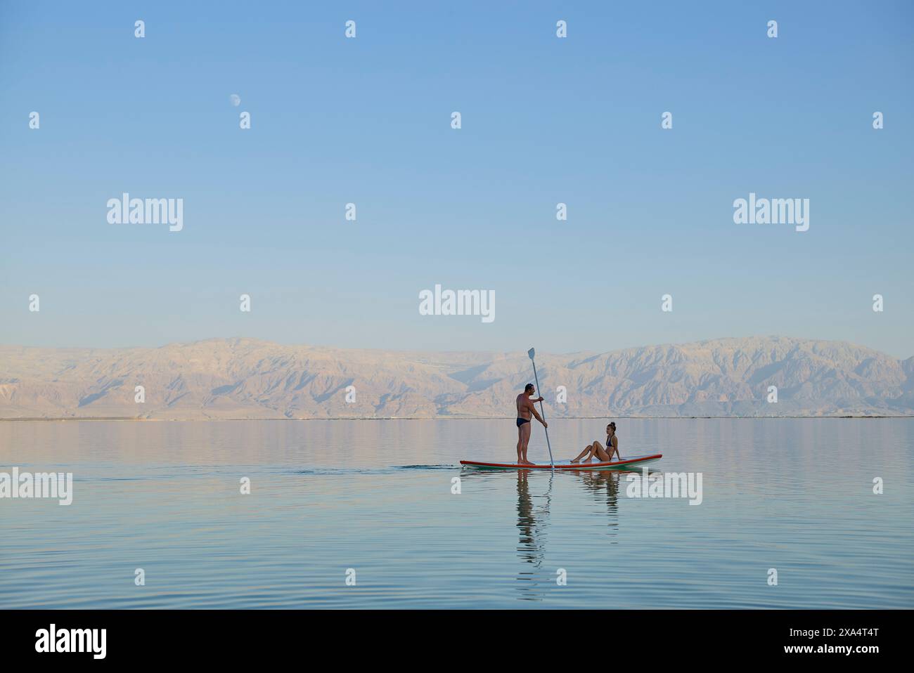 Due persone pagaiano su un lago calmo con montagne lontane sotto un cielo limpido. Foto Stock