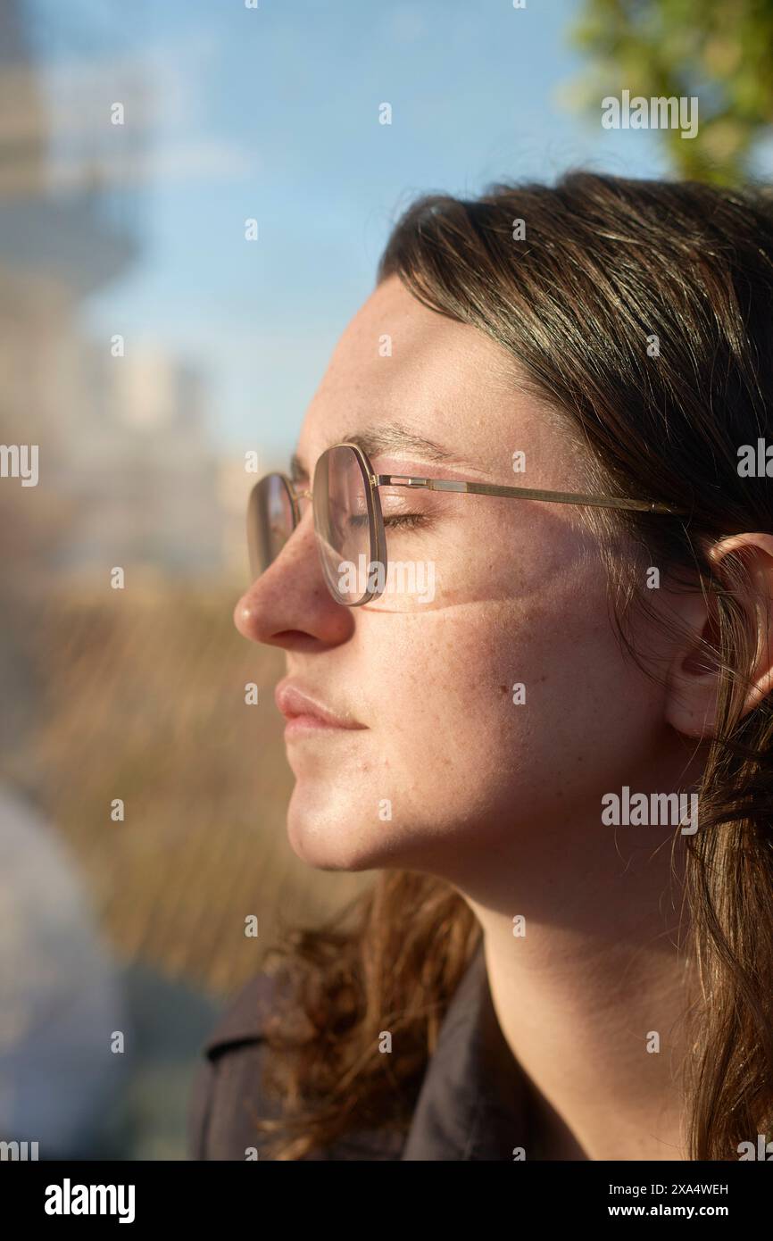 Profilo laterale di una giovane donna con occhiali che si gode il sole a occhi chiusi. Foto Stock