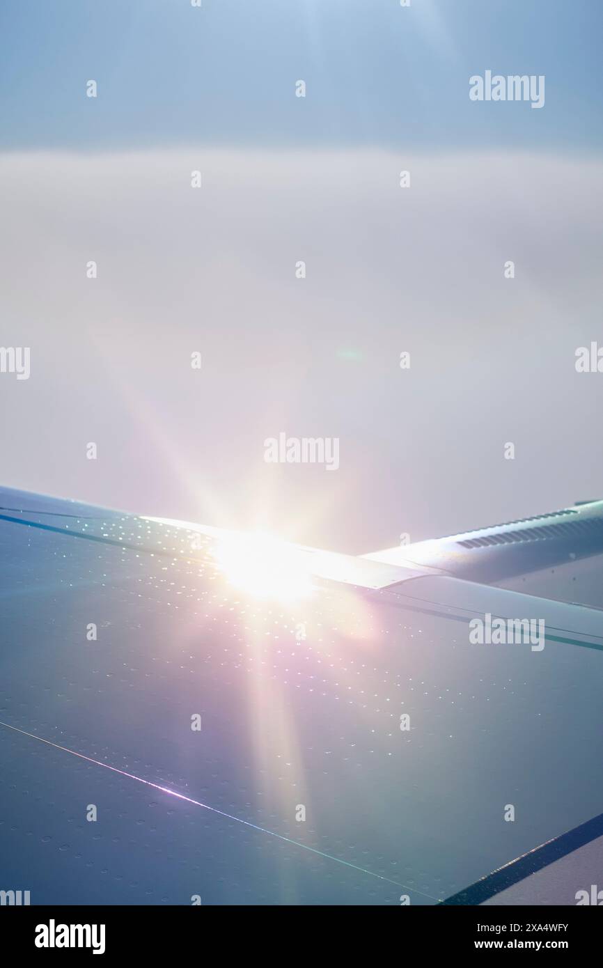 La luce del sole splende sopra un'ala di un aeroplano contro un cielo blu chiaro durante il volo. Foto Stock