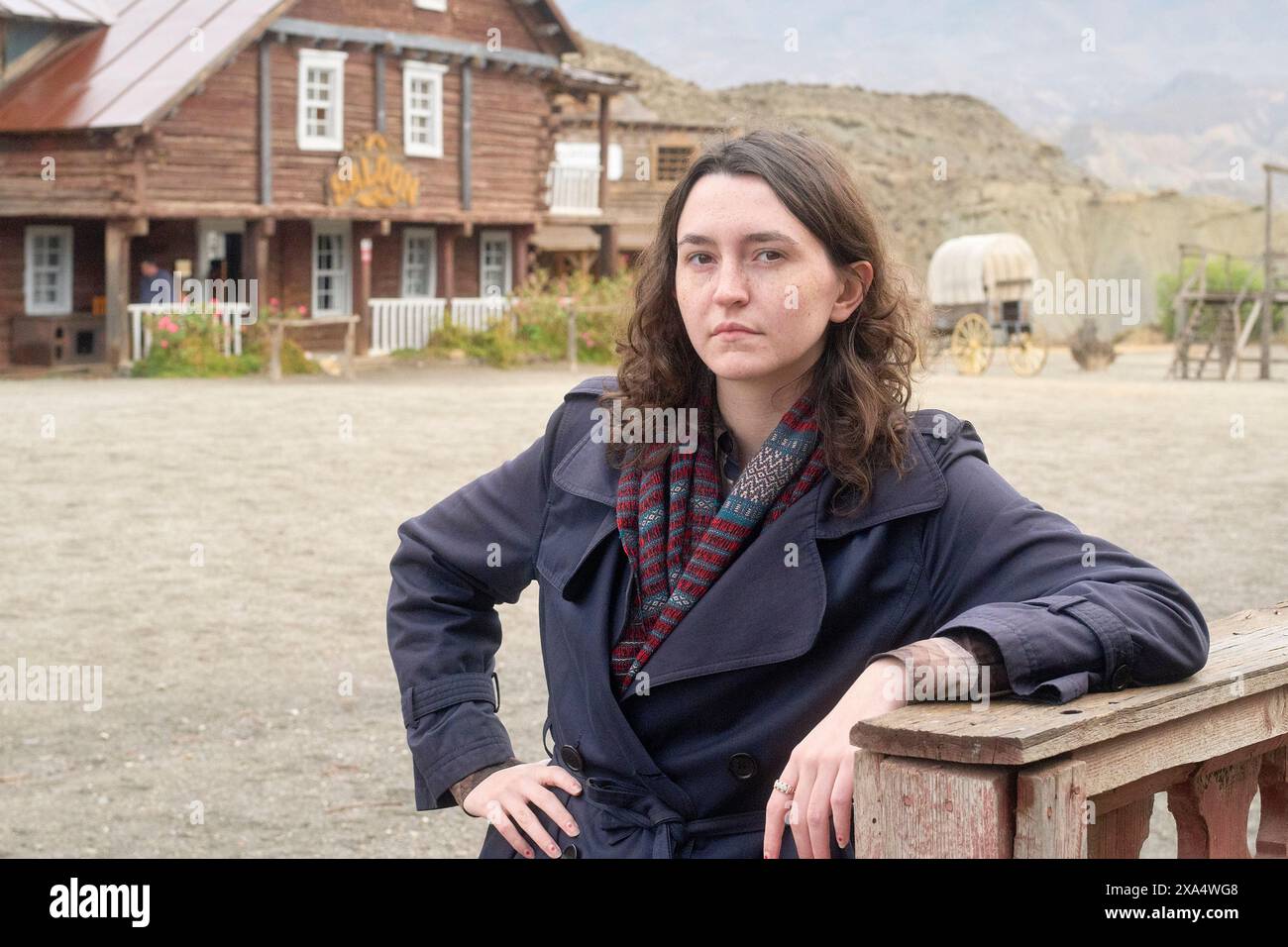 Donna sicura di sé appoggiata su una recinzione in legno in un ambiente urbano in stile western con un'espressione premurosa. Foto Stock Donna sicura di sé appoggiata su una recinzione in legno in un ambiente urbano in stile western con un'espressione premurosa. Foto Stock