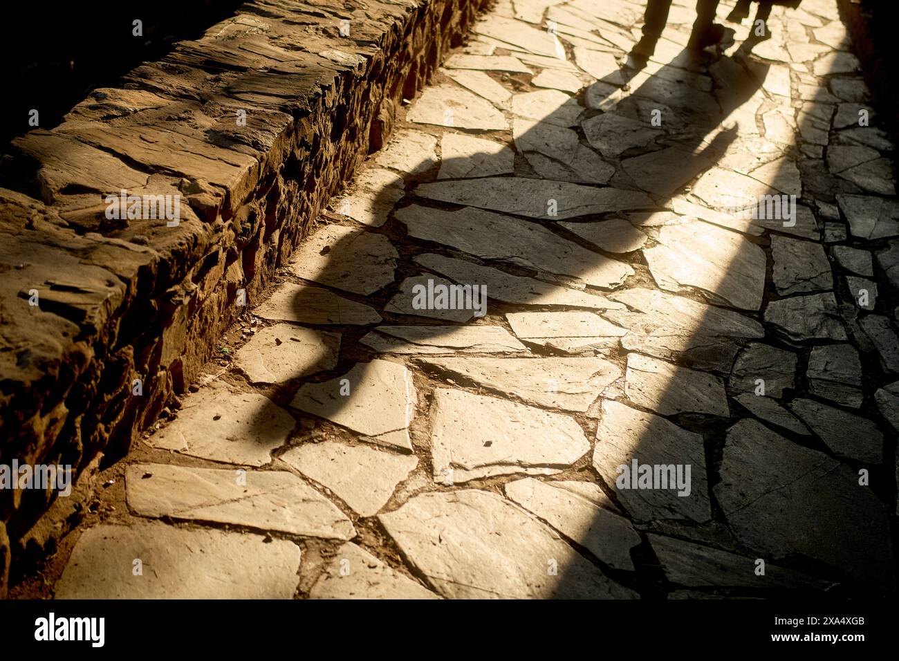 La luce del sole proietta le ombre delle persone su un sentiero di pietra irregolare. Foto Stock