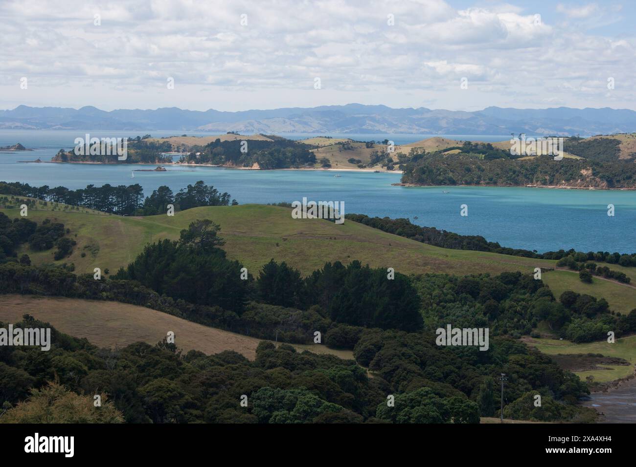 Vista panoramica di un paesaggio costiero con lussureggianti colline verdi e una tranquilla baia blu sotto un cielo parzialmente nuvoloso. Foto Stock