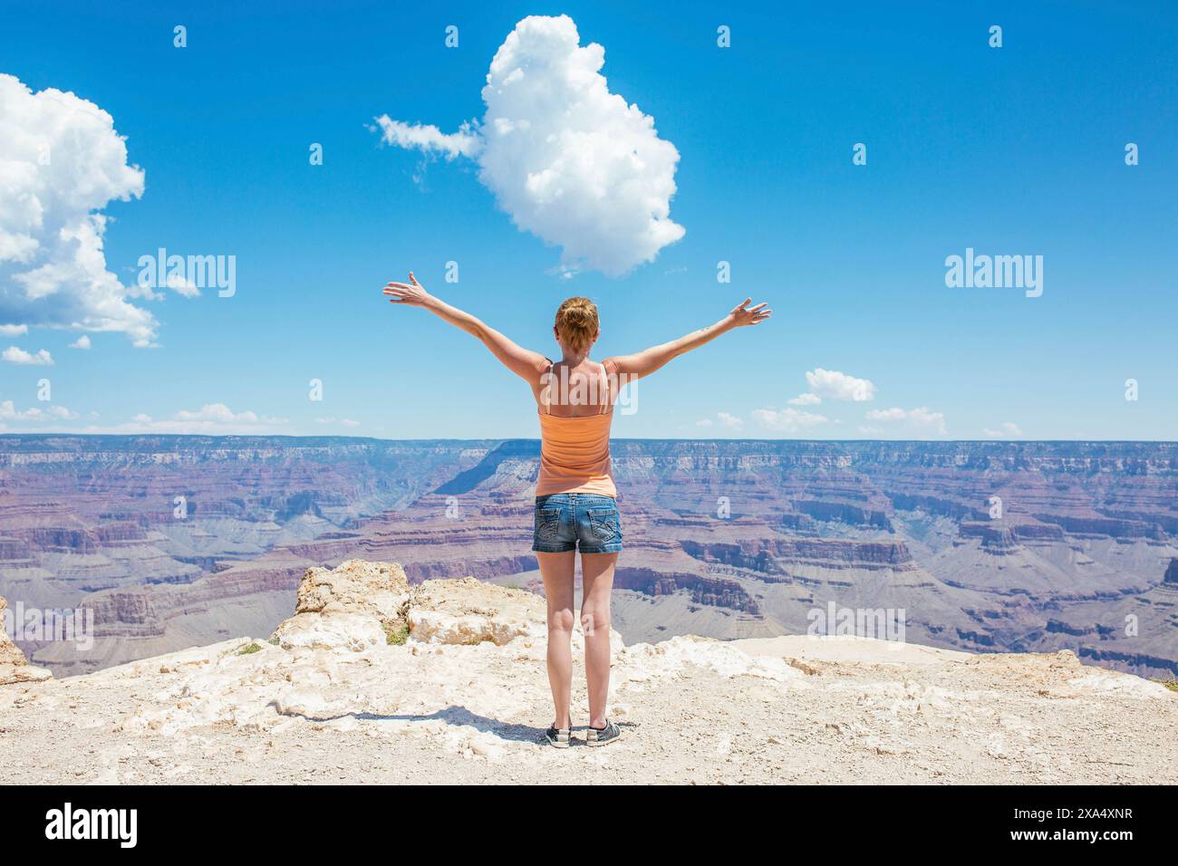 Donna con le braccia spalancata in piedi ai margini del Grand Canyon sotto un cielo blu. Foto Stock