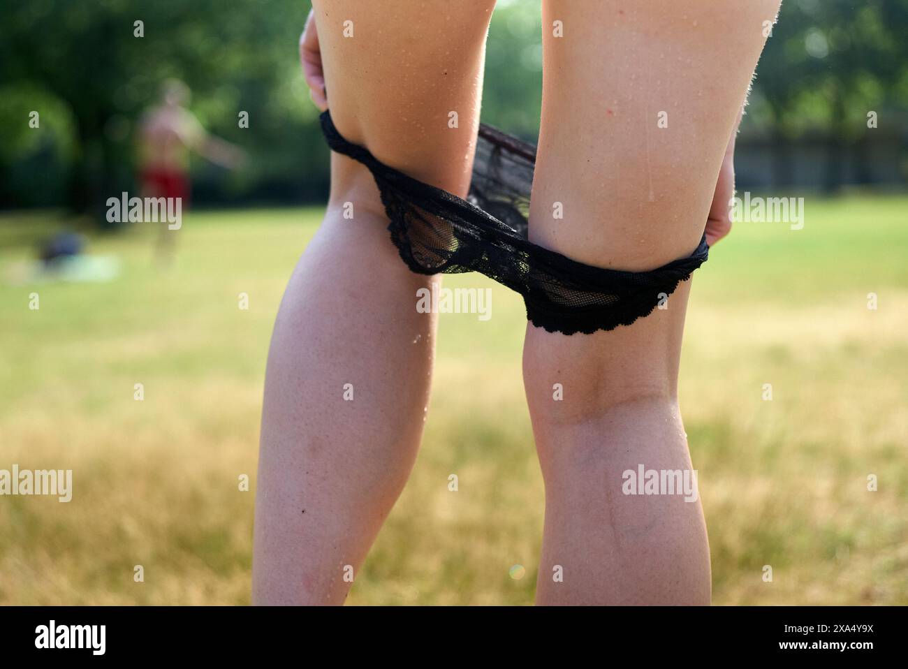 Primo piano di una persona che tira calze nere al ginocchio in una giornata di sole in un parco erboso con persone sullo sfondo. Foto Stock