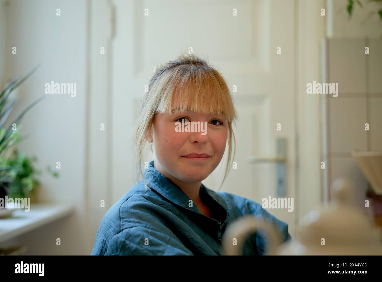 Primo piano di una giovane donna sorridente con capelli biondi che indossa una camicia in denim in un ambiente domestico. Foto Stock