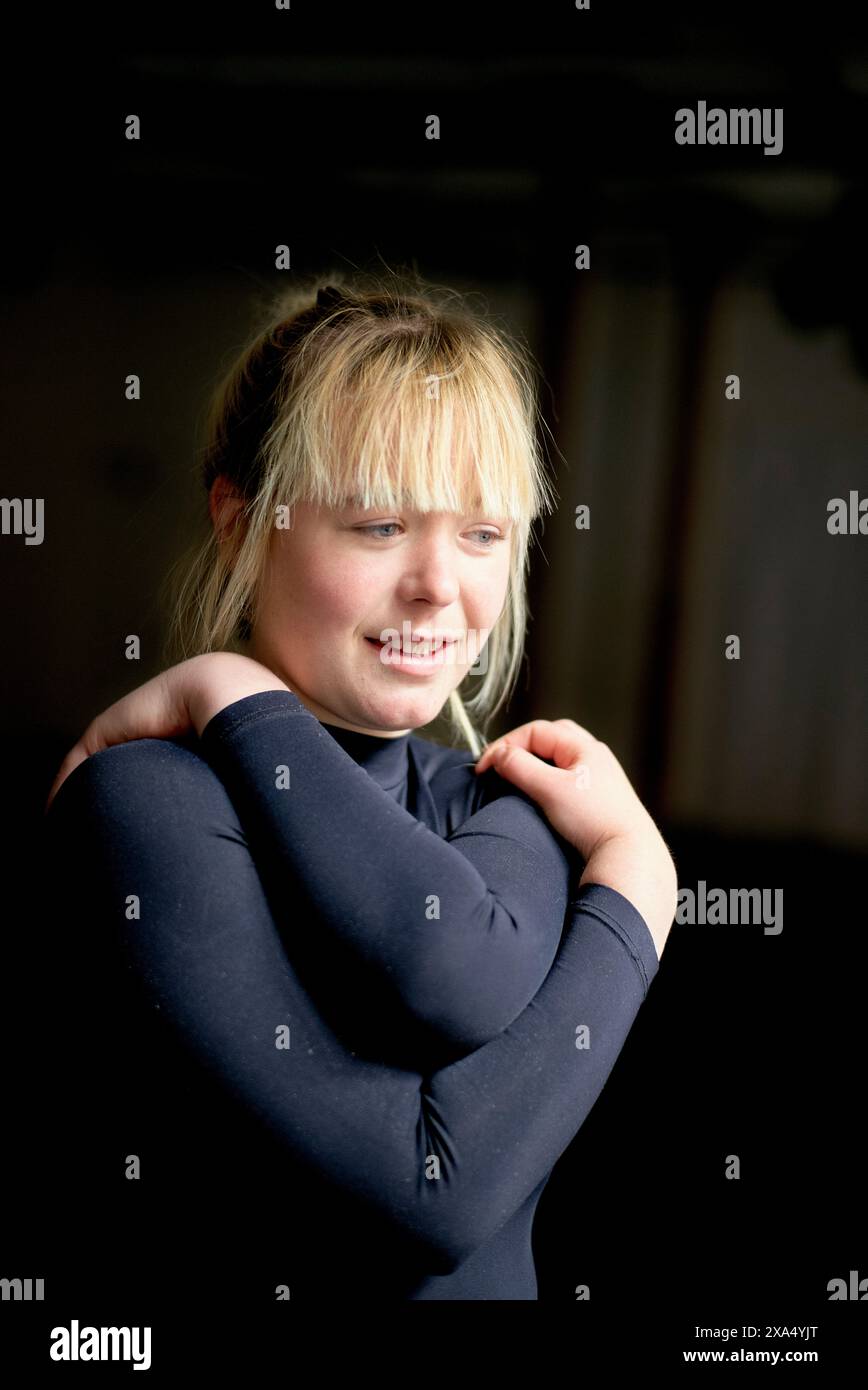 Giovane donna sorridente con capelli biondi che indossa un top scuro che guarda di lato. Foto Stock