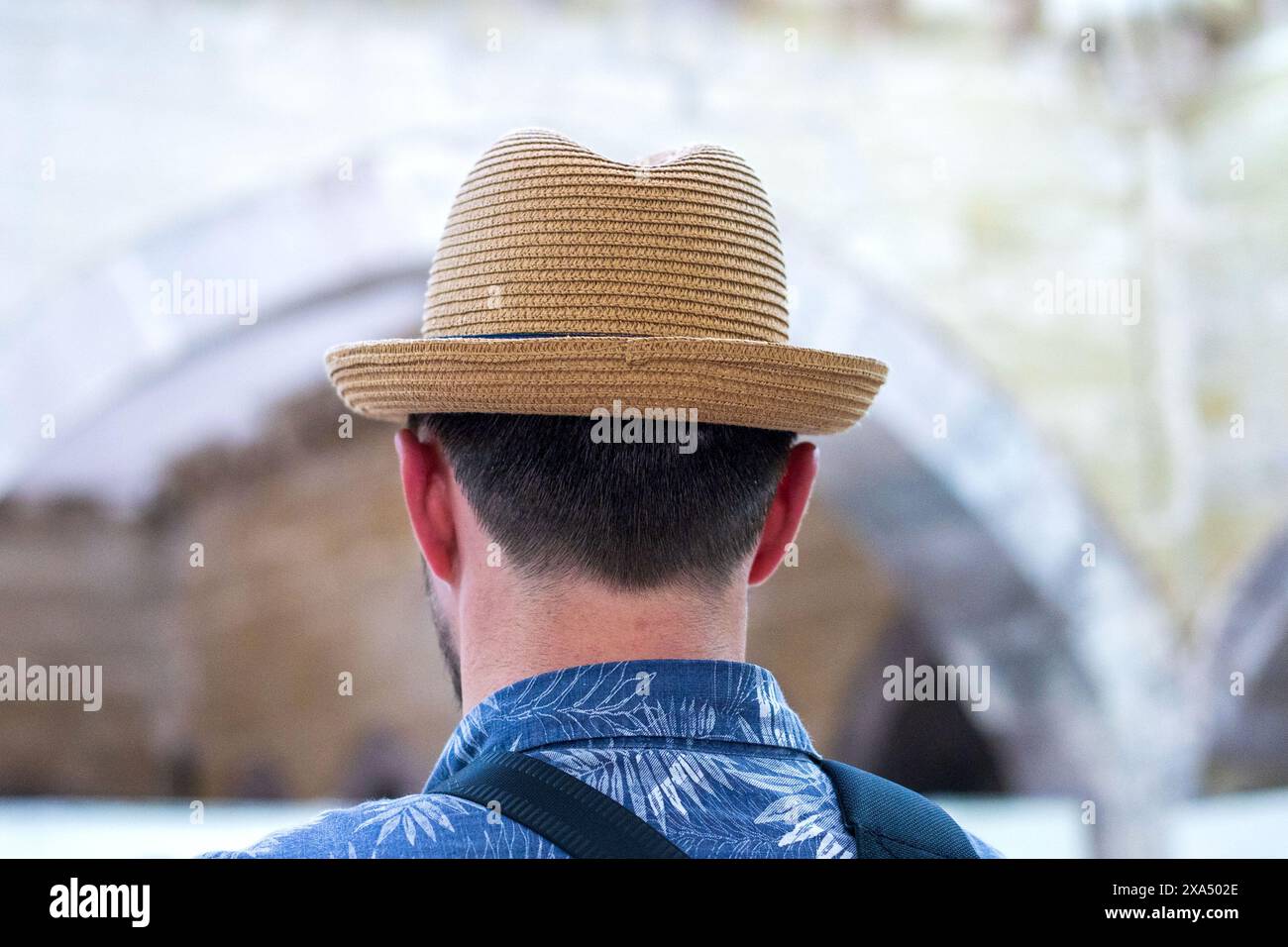 Giovane uomo con cappello di paglia cachi incorniciato da un'antica cornice ad arco: Una prospettiva turistica, vista posteriore. Foto Stock